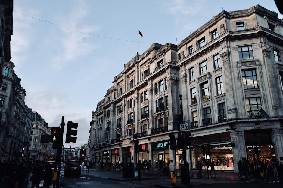 A busy street scene in an urban environment featuring a diverse group of pedestrians crossing a wide crosswalk, with some individuals engaged in conversation and others walking purposefully. In the fo